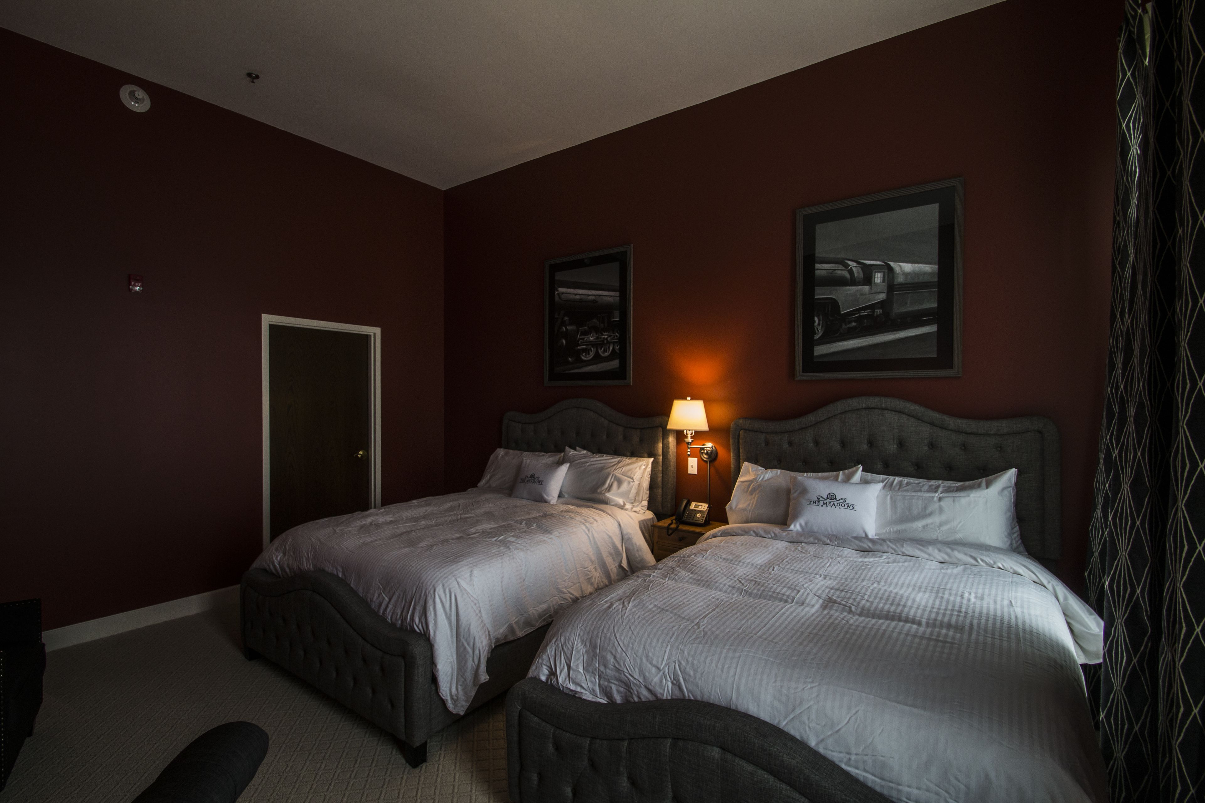 Habitación de hotel con dos camas, una mesita de noche con lámpara y dos cuadros enmarcados en la pared.