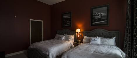 Habitación de hotel con dos camas, una mesita de noche con lámpara y dos cuadros enmarcados en la pared.