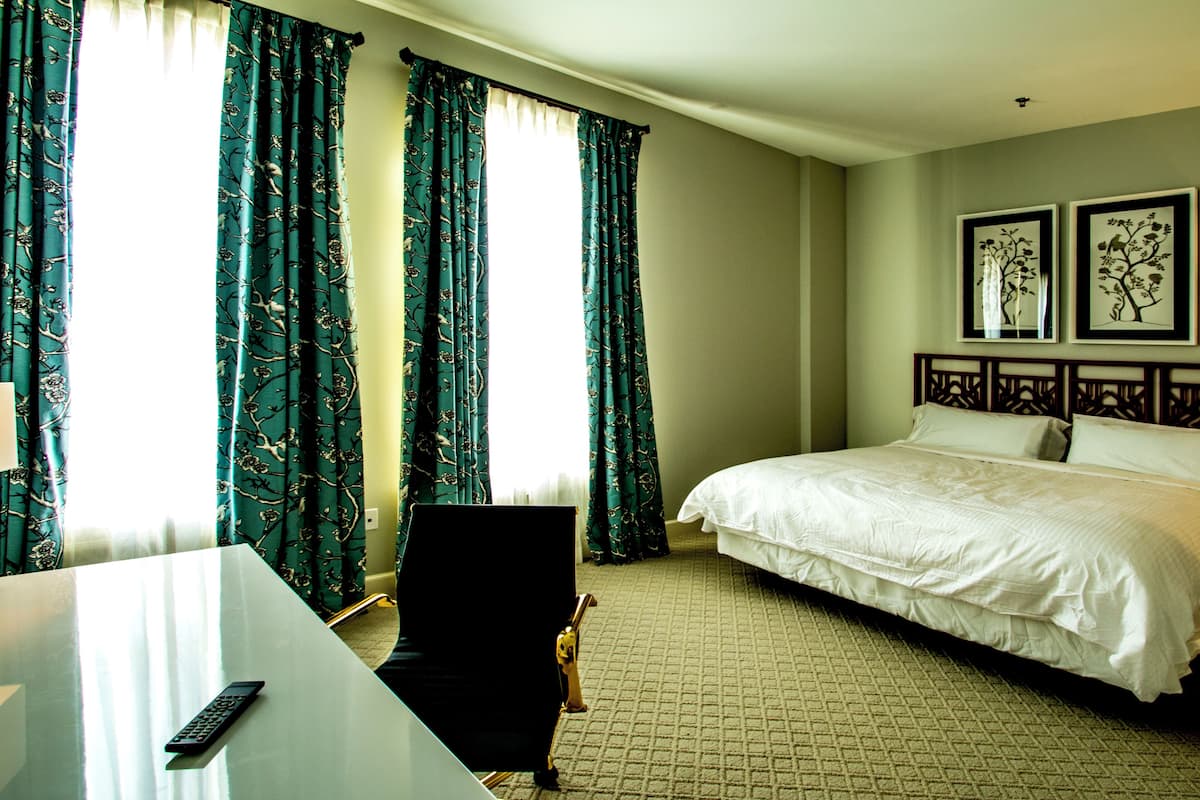A hotel room with a bed, a desk, a chair, and curtains.