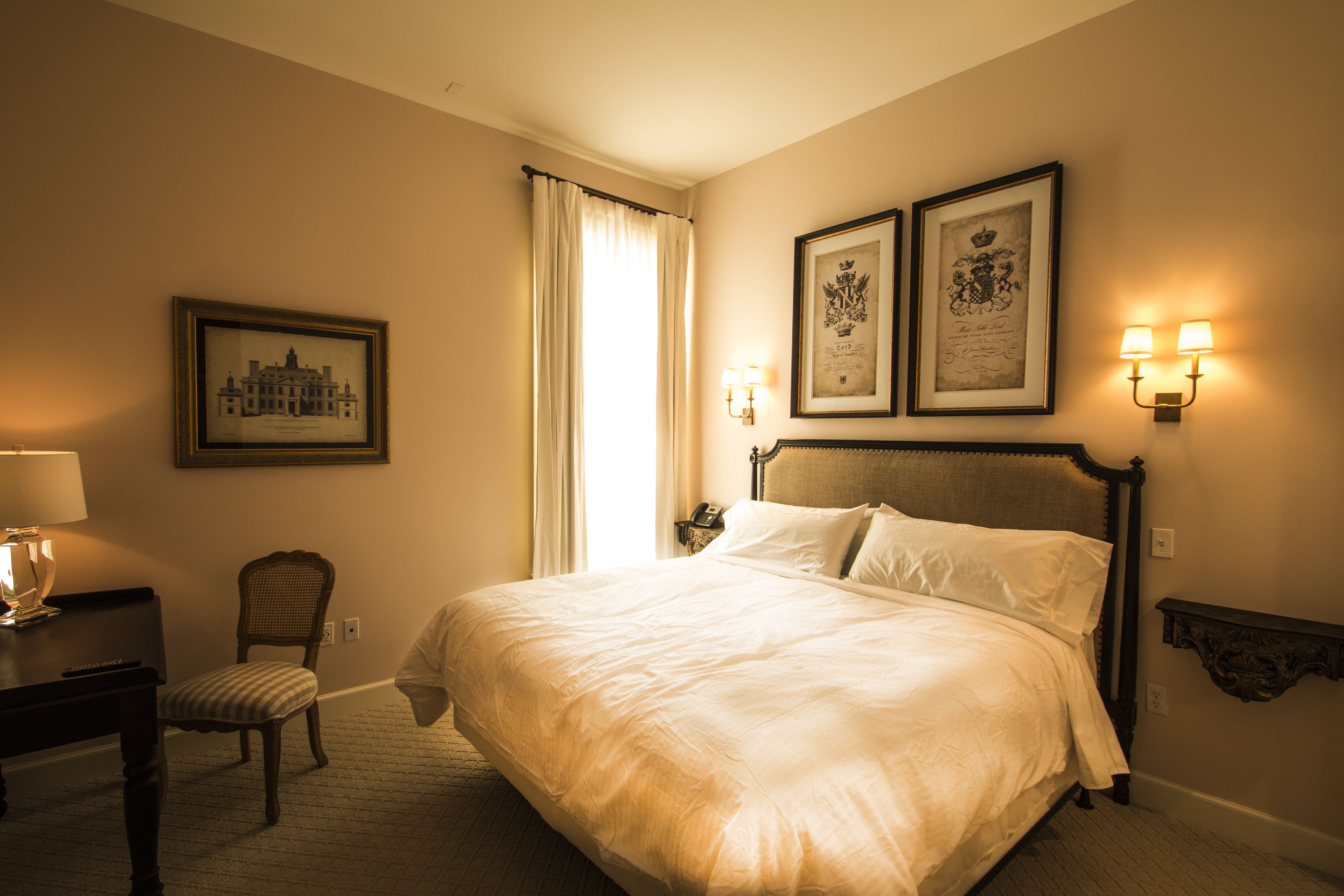 Habitación de hotel con una cama grande, una silla, un escritorio con lámpara y dos cuadros en la pared.