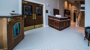 A reception area with a wooden desk labeled 'Bellman', a patterned floor, and a staircase leading to another floor. - The Meadows Hotel (Fulton)