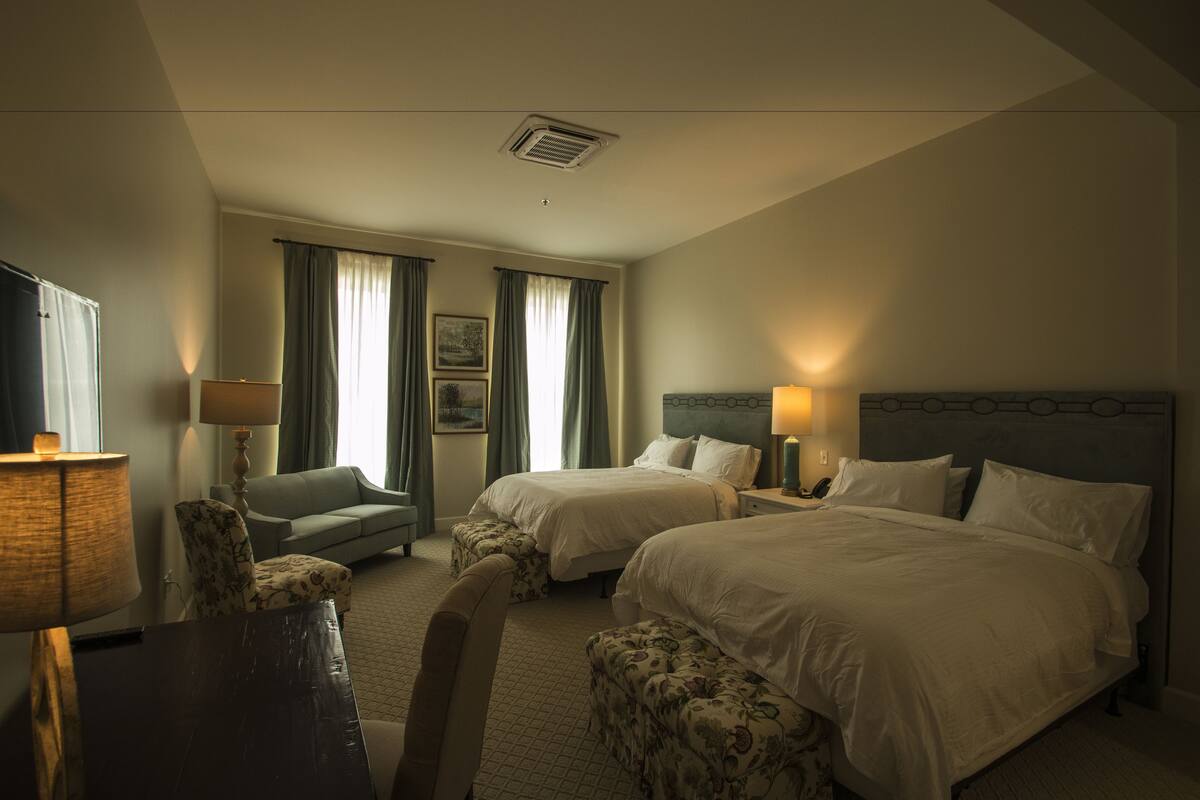 A hotel room with two beds, a sofa, a desk, and a lamp.