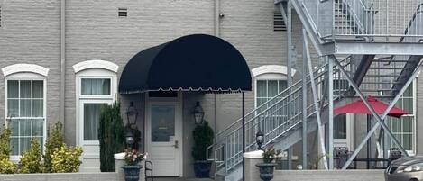 Un bâtiment à deux étages, doté d’une façade grise, d’un auvent noir au-dessus de l’entrée et d’un escalier menant à un niveau supérieur.