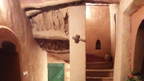Un intérieur rustique avec un escalier, une chaise sur laquelle est posé un chapeau et une plante en pot.