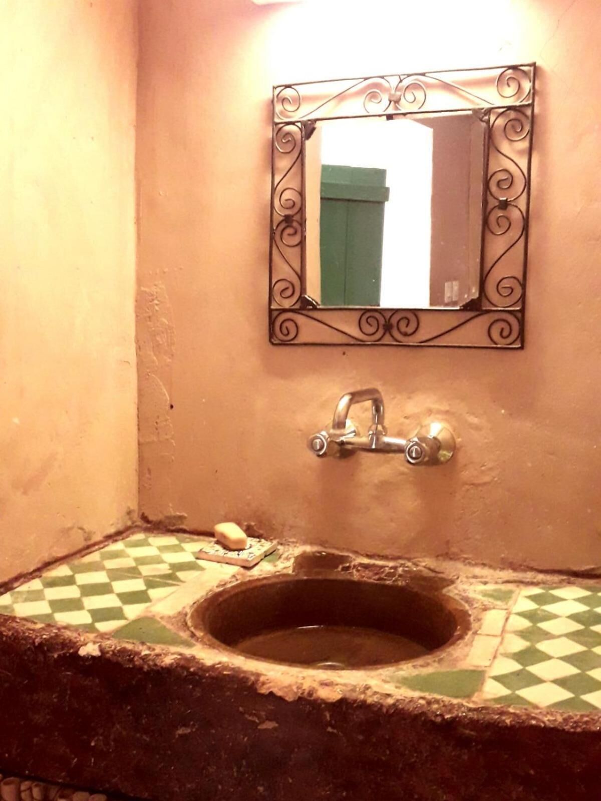 A bathroom with a checkered floor, a sink with a greenish basin, and a mirror with ornate metal framing.