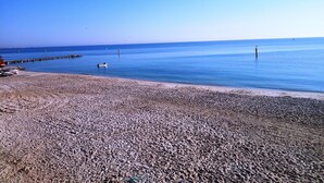 Una playa pedregosa con un mar tranquilo, un bote pequeño y un muelle que se adentra en el agua.