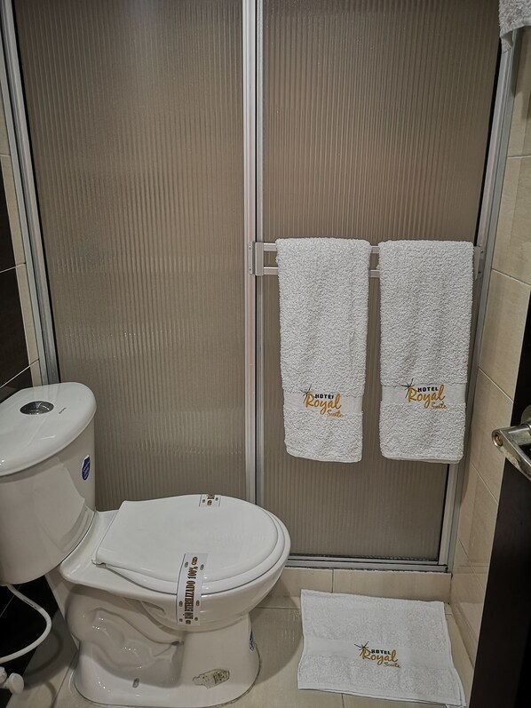 A bathroom with a toilet, a shower, and two towels hanging on a rack with the text "HOTEL Royal Suite". - Hotel Royal Suite (Manizales)