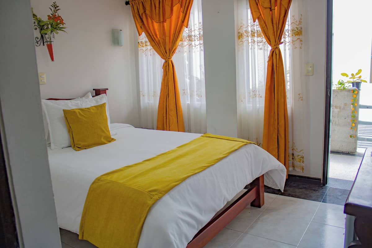 A hotel room with a bed, curtains, and a potted plant.