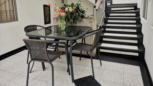 A dining area with a glass table and wicker chairs, a potted plant with flowers, and a black and white staircase. - Hotel Royal Suite (Manizales)