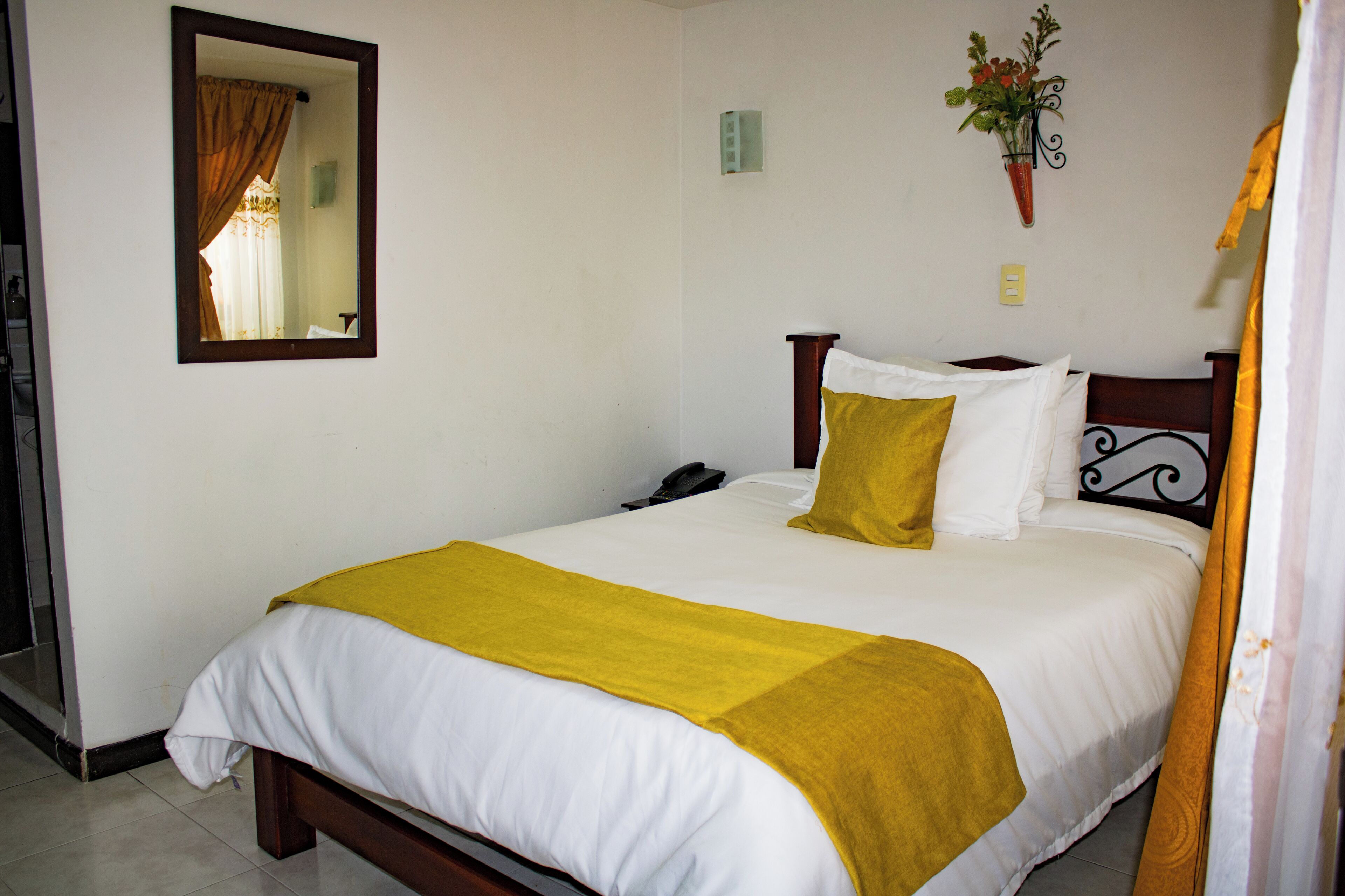 A neatly made bed with white and yellow bedding, a wooden headboard, and a mirror on the wall.
