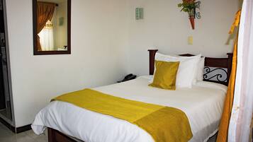 A neatly made bed with white and yellow bedding, a wooden headboard, and a mirror on the wall.