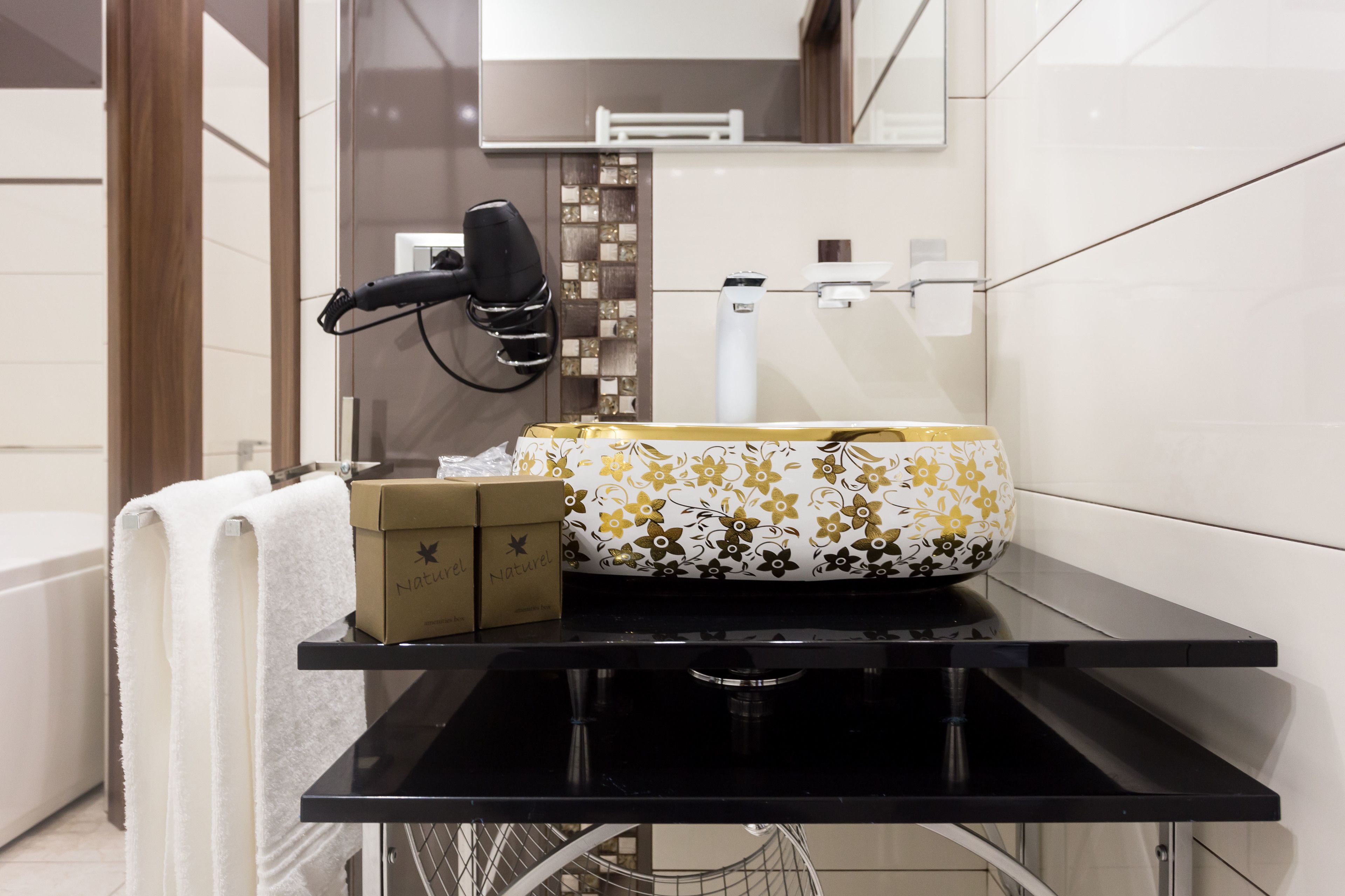 Een badkamer met een zwart aanrechtblad, een witte handdoek, een doosje met de tekst 'Naturel' en een wastafel met bloemenmotief.