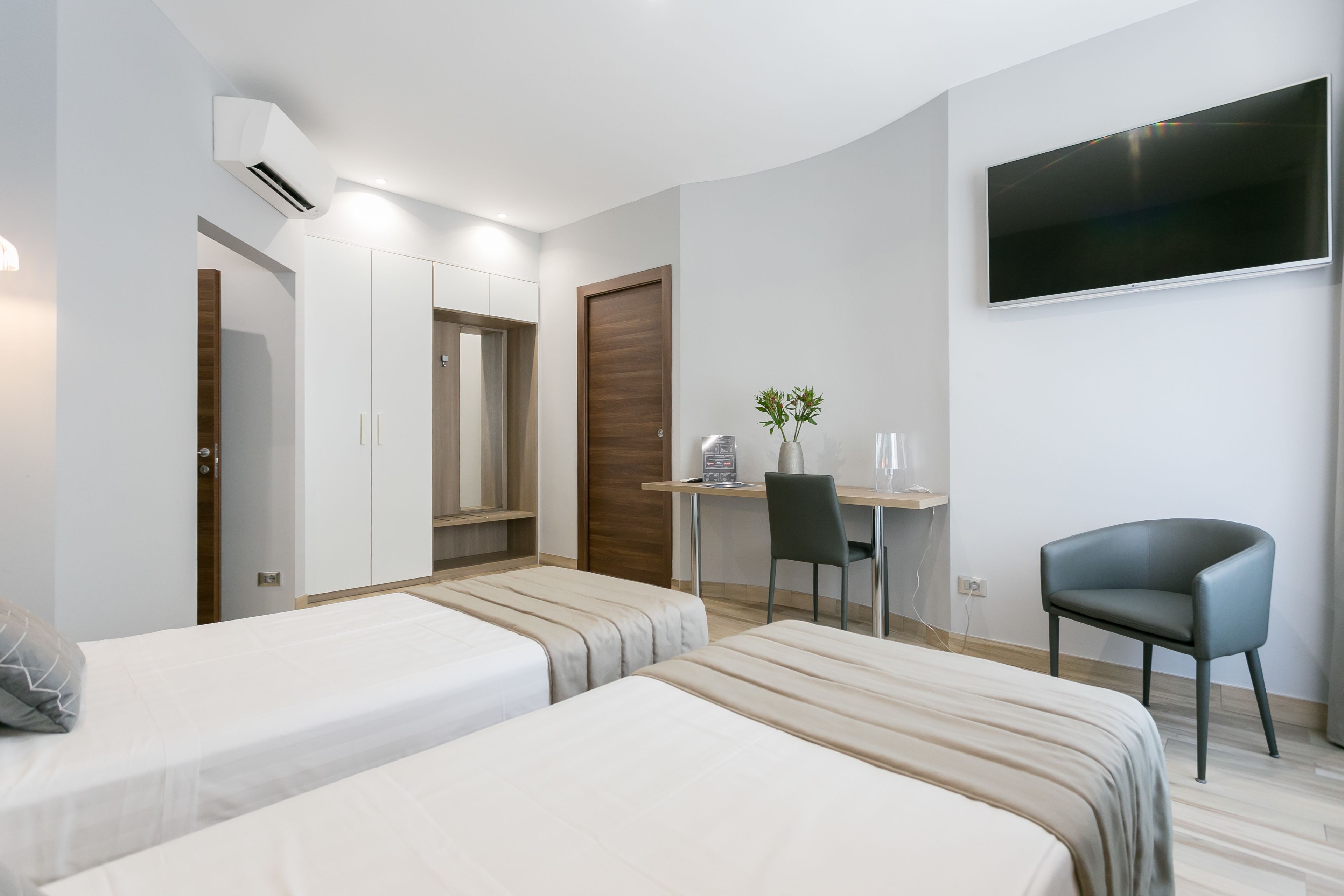 Ein modernes Hotelzimmer mit zwei Betten, einem Schreibtisch, einem Sessel, einem Fernseher und einem Kleiderschrank.