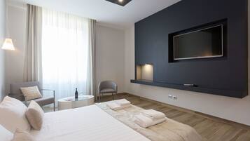 Une chambre d’hôtel moderne dotée d’un grand lit, d’un téléviseur à écran plat fixé au mur, d’un coin salon avec une chaise et une table, et d’une grande fenêtre avec des rideaux.