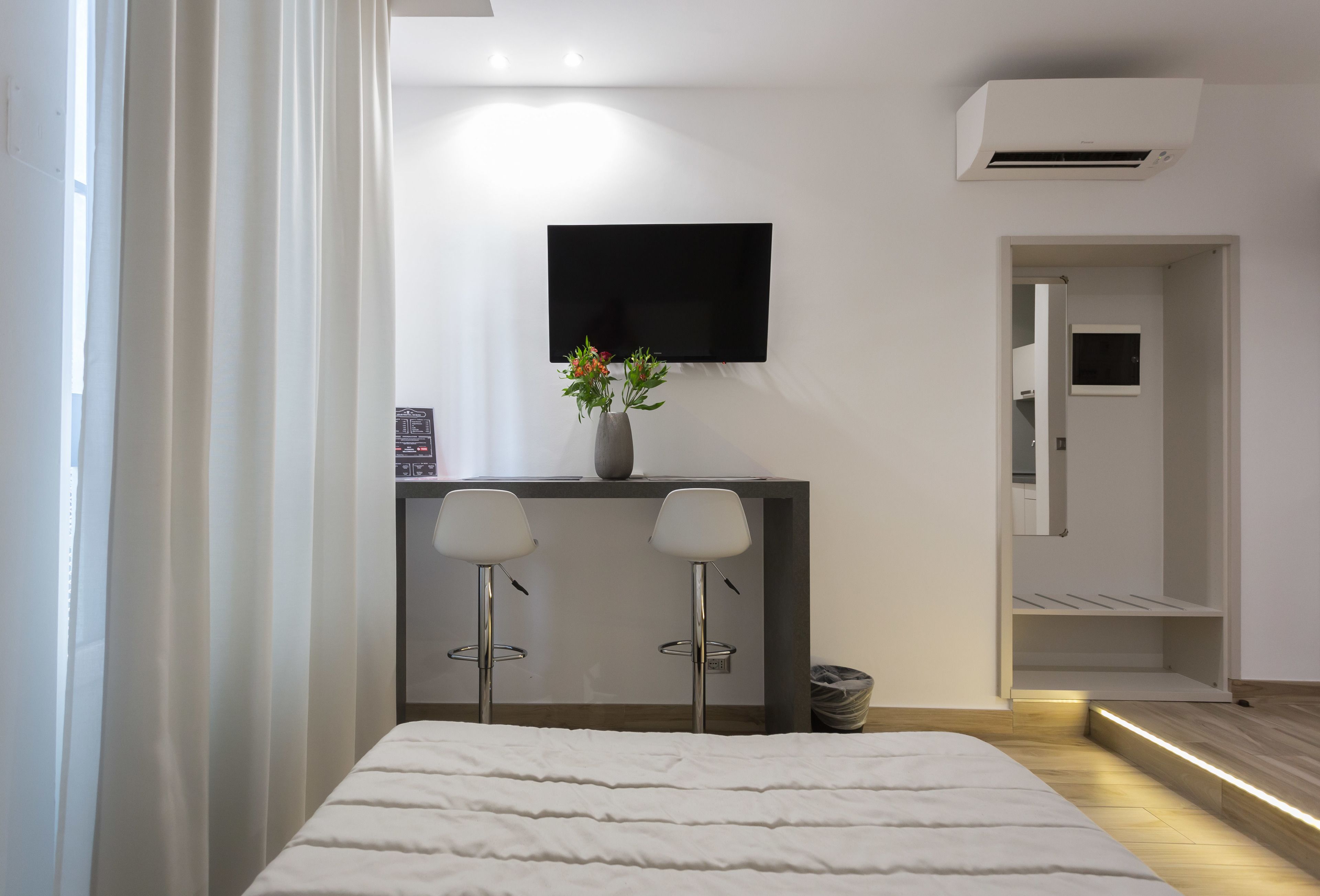 Un dormitorio moderno con una cama, un escritorio con dos sillas, un televisor y una planta peque ña.