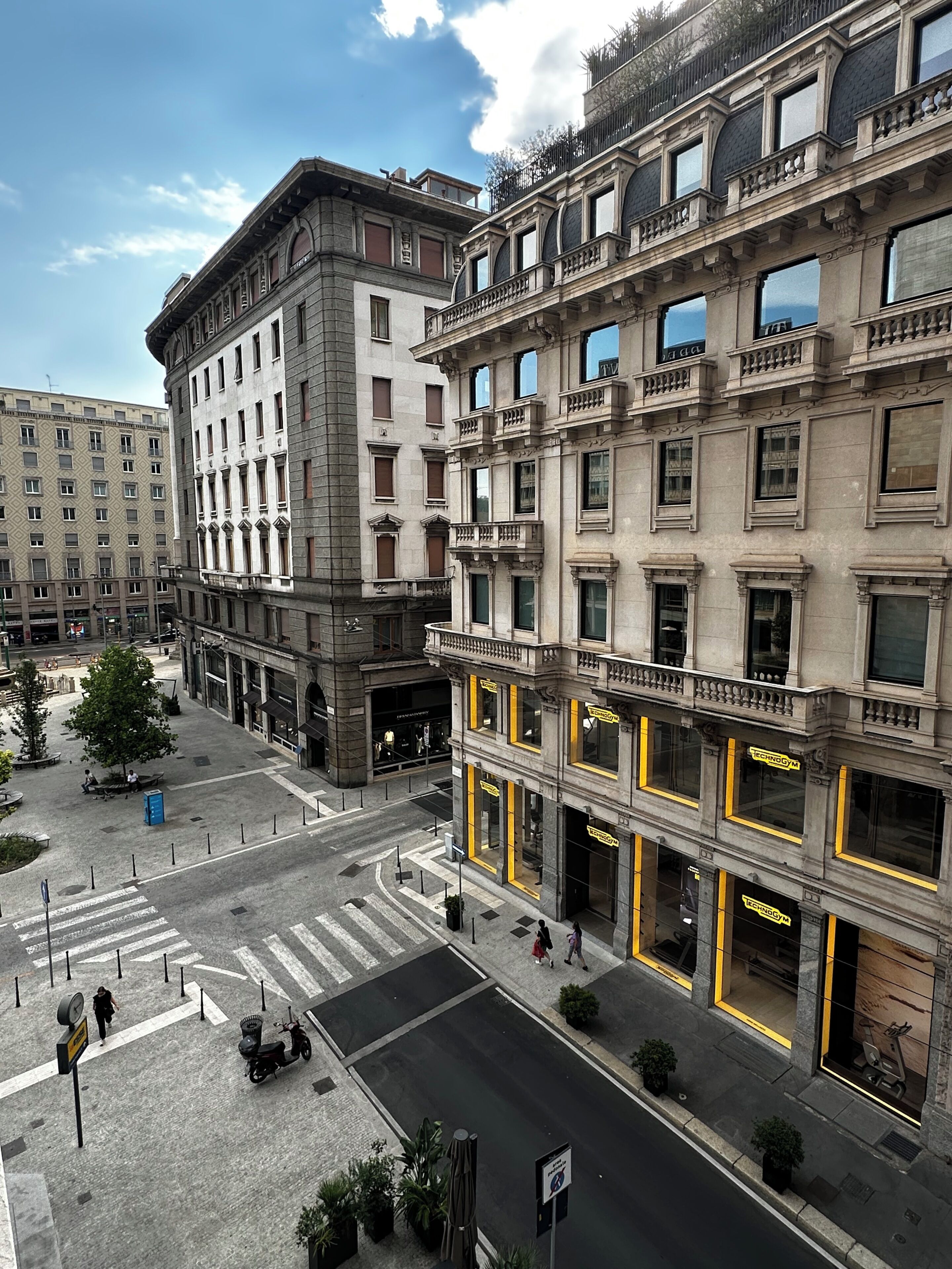 A multi-story building with a ground-floor entrance, a pedestrian crossing, and a street with a scooter parked.