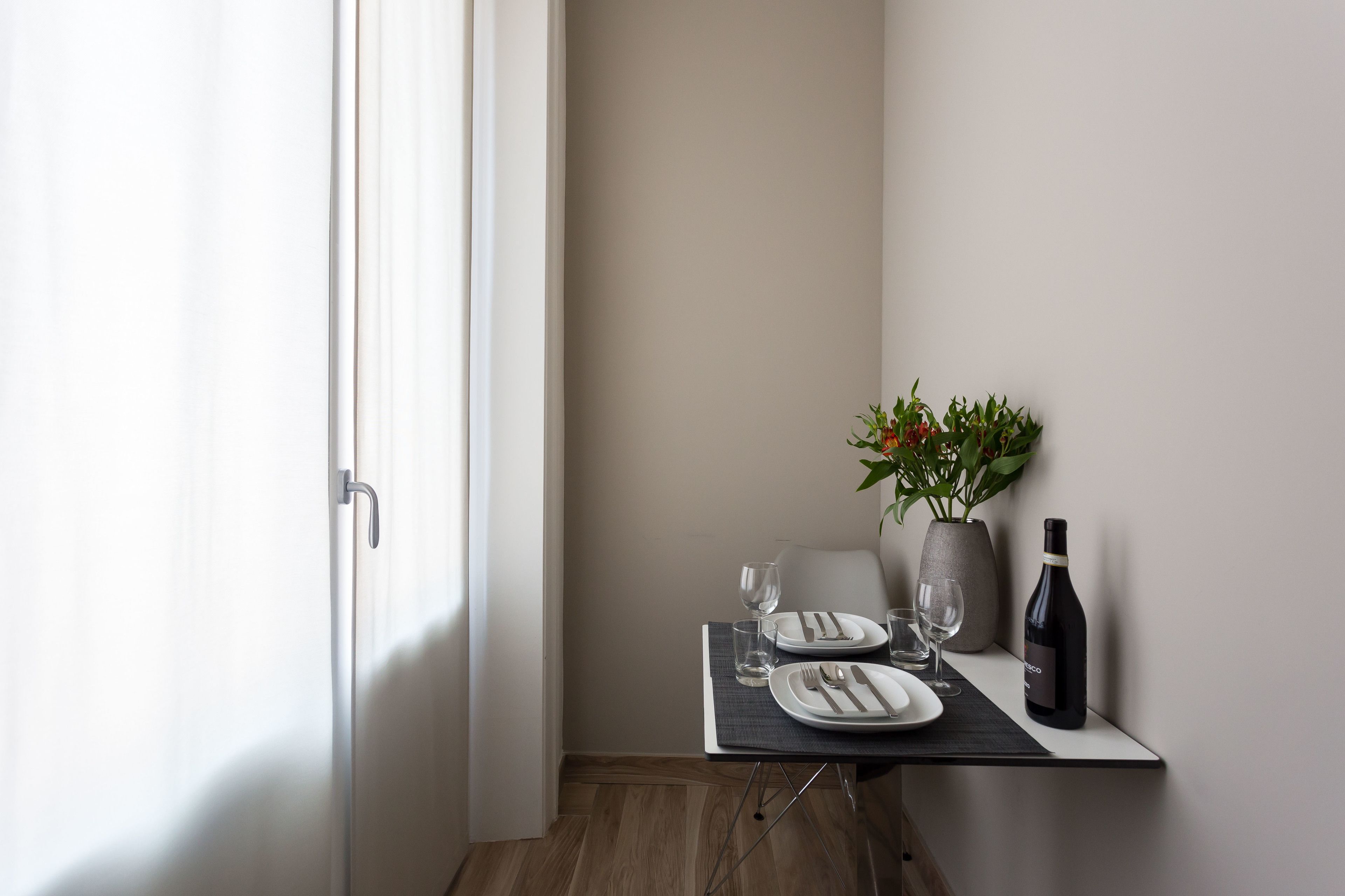 A neatly arranged dining area with a table set for two, a vase with flowers, and a bottle of wine.