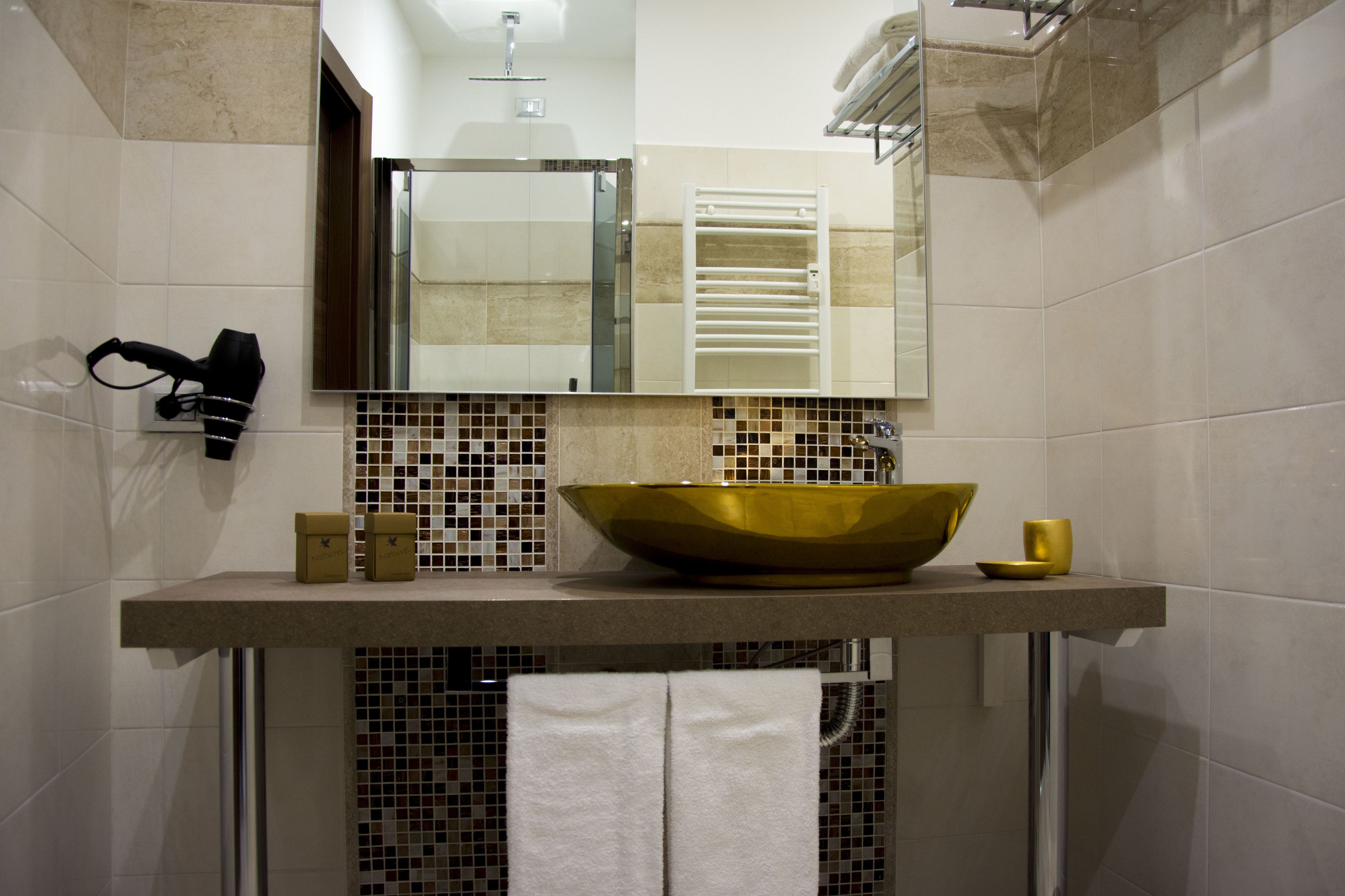 Un baño con un lavamanos grande de color dorado, un espejo encima y un perchero con toallas.