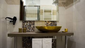Un baño con un lavamanos grande de color dorado, un espejo encima y un perchero con toallas.