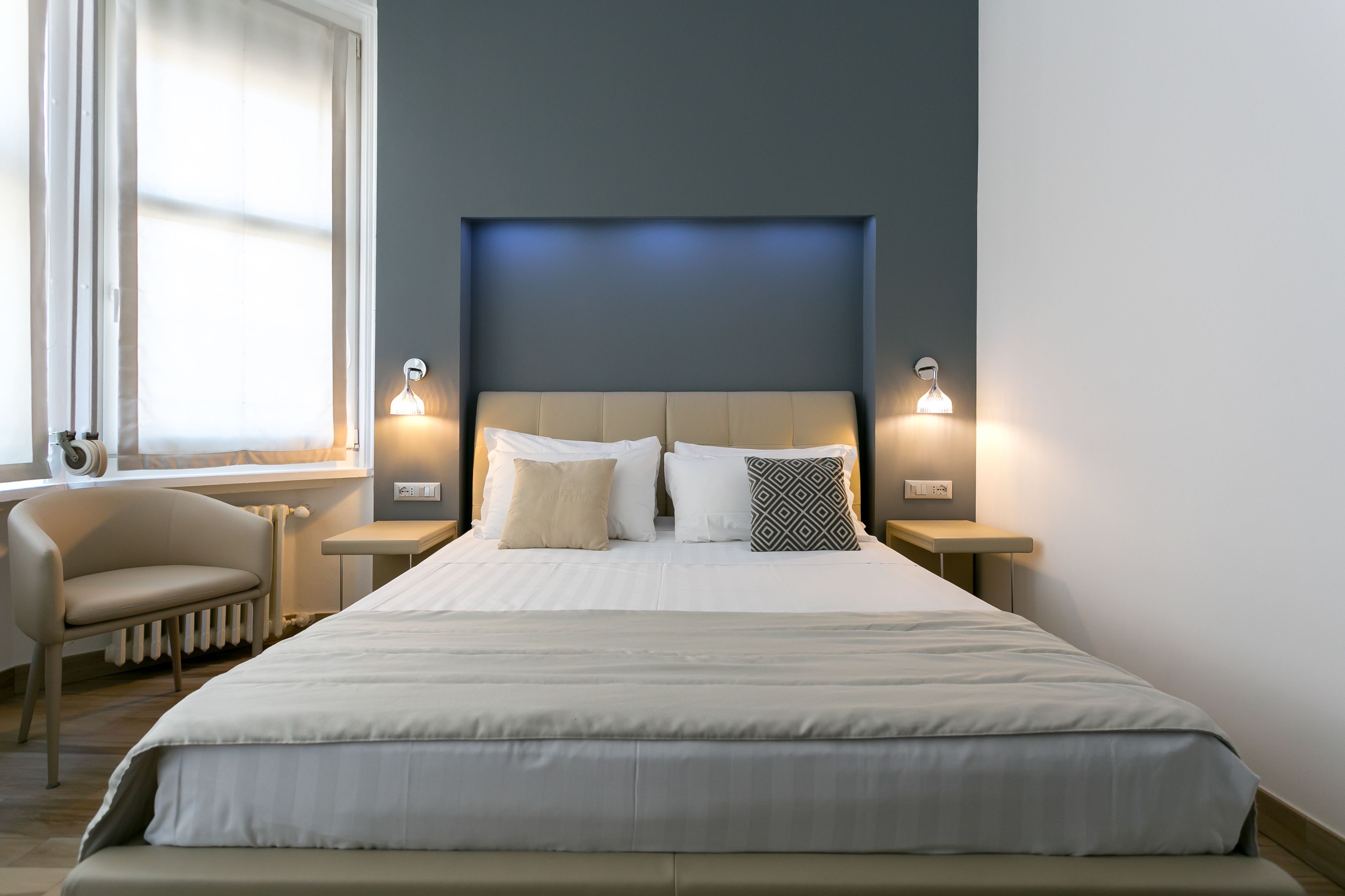 Camera d'albergo moderna con un letto grande, due comodini, una sedia e una finestra con tende.