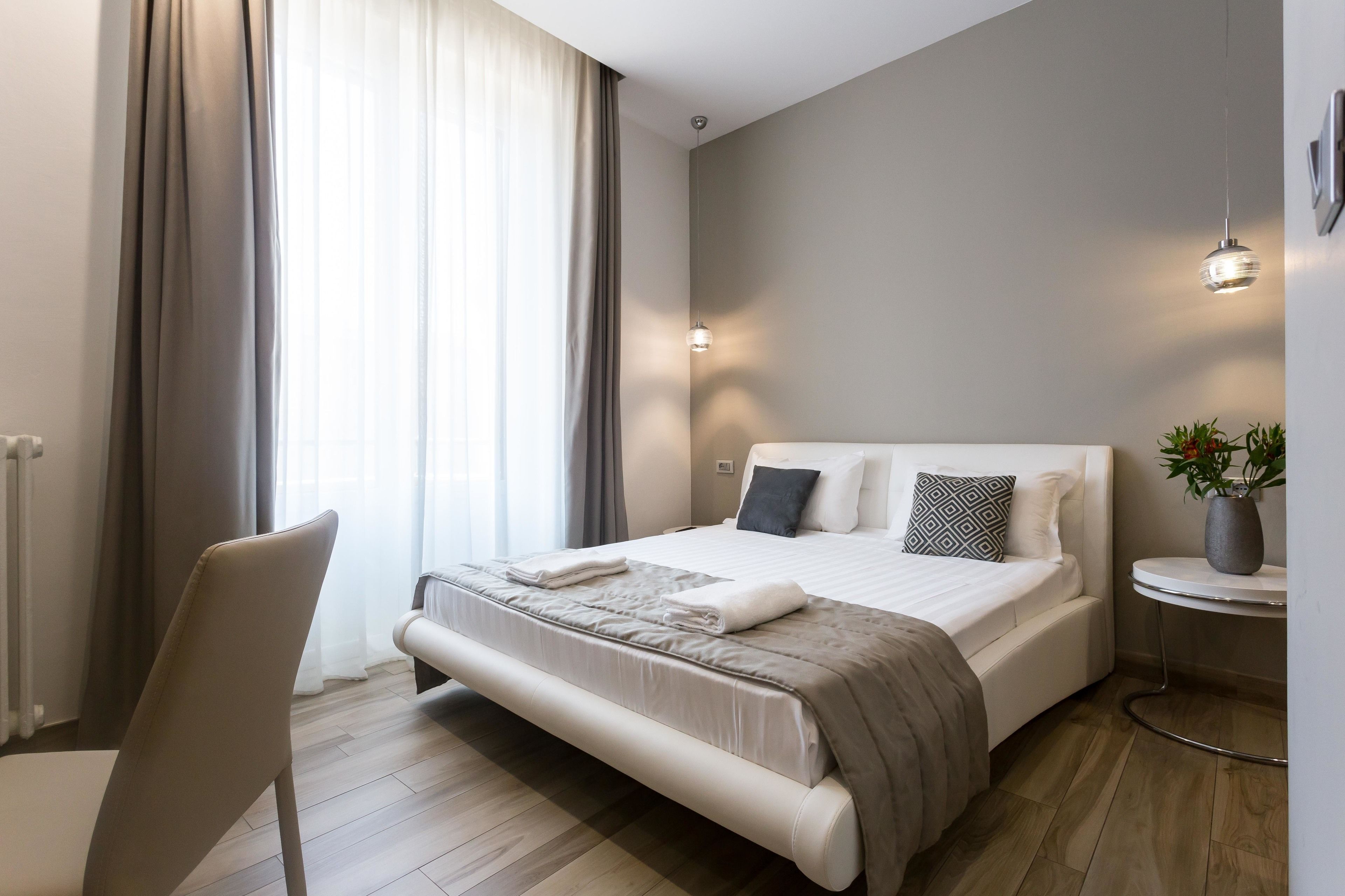Ein modernes Schlafzimmer mit einem großen Bett, einem Sessel, einem kleinen Tisch und einer Topfpflanze.