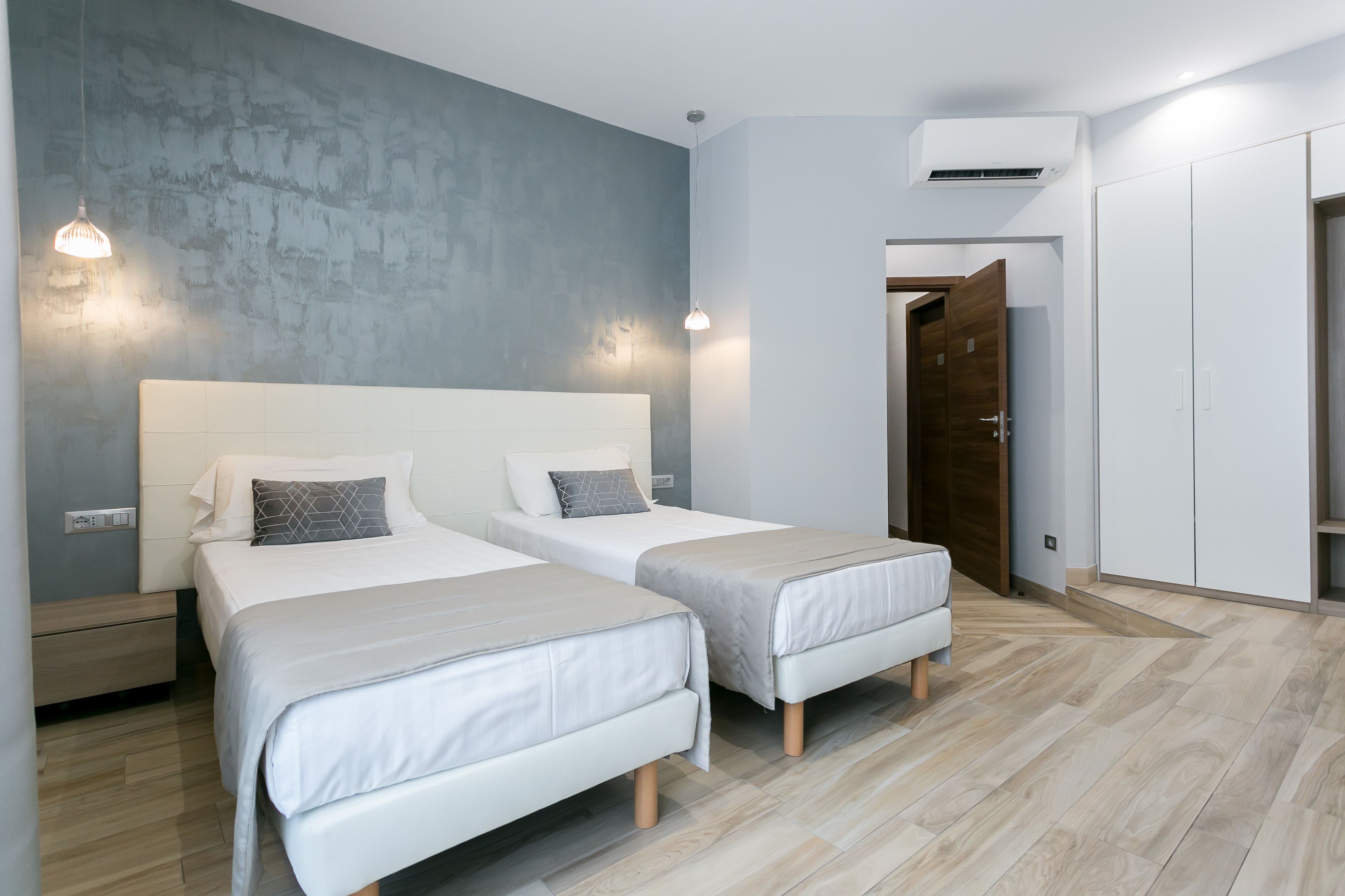 Quarto moderno com duas camas, parede de destaque em concreto e um guarda-roupa.