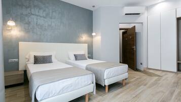 Quarto moderno com duas camas, parede de destaque em concreto e um guarda-roupa.