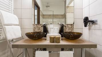 Une salle de bain avec deux grands lavabos en verre, un porte-serviettes, un sèche-cheveux et un miroir.