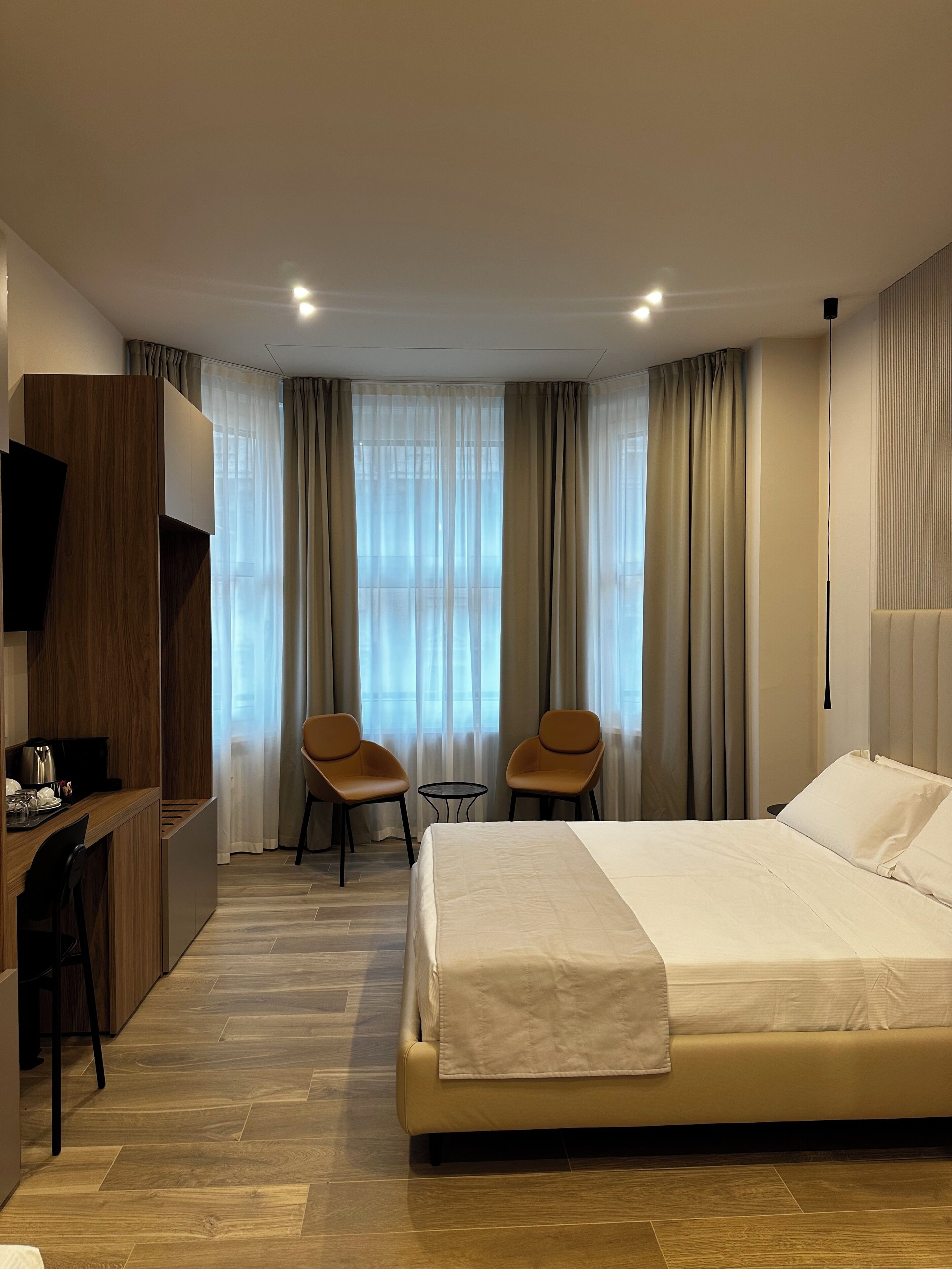 A hotel room with a bed, two chairs, a desk with a chair, a television, and a window with curtains.