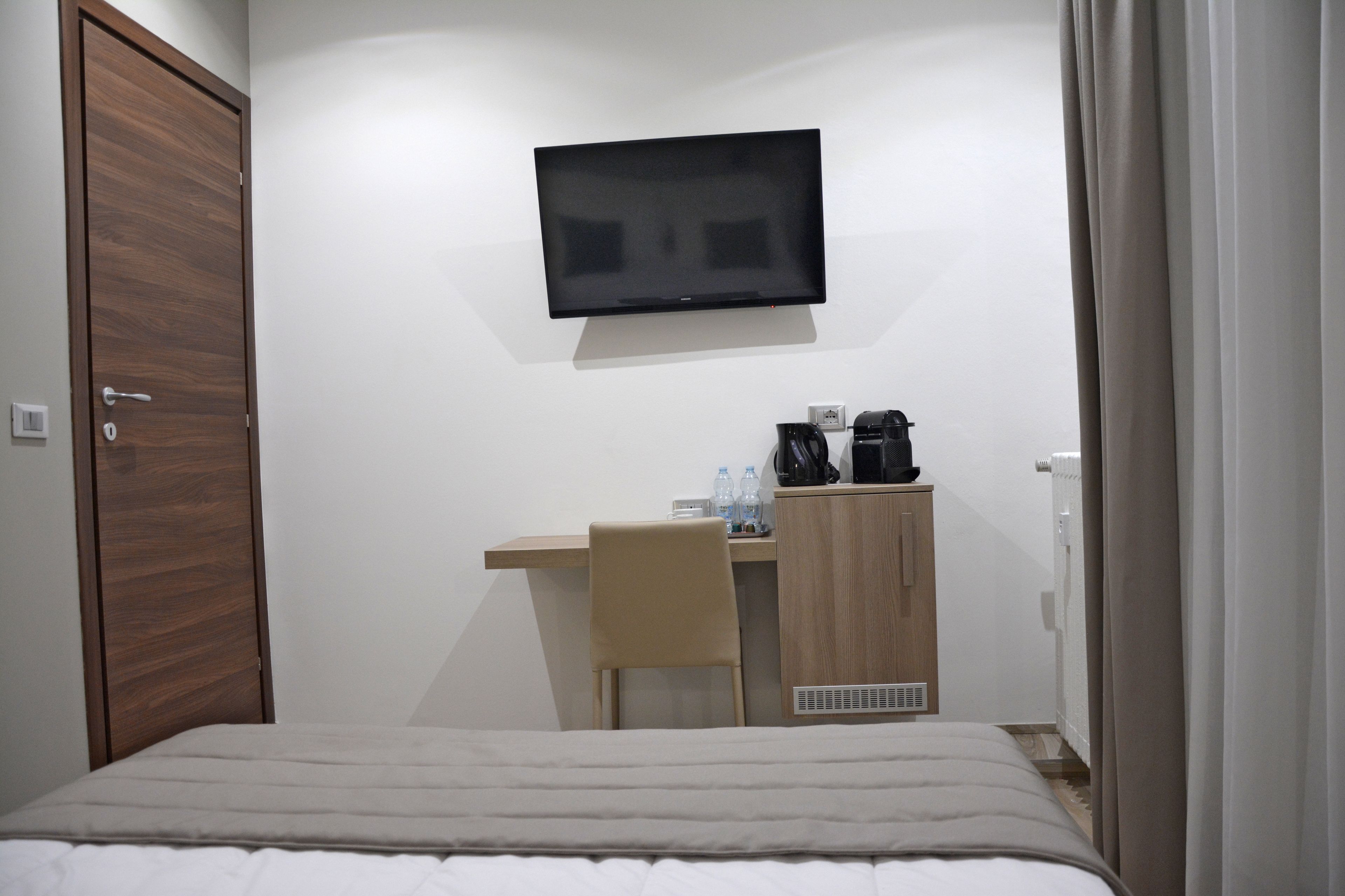 A hotel room with a bed, a desk, a chair, a television, and a wardrobe.