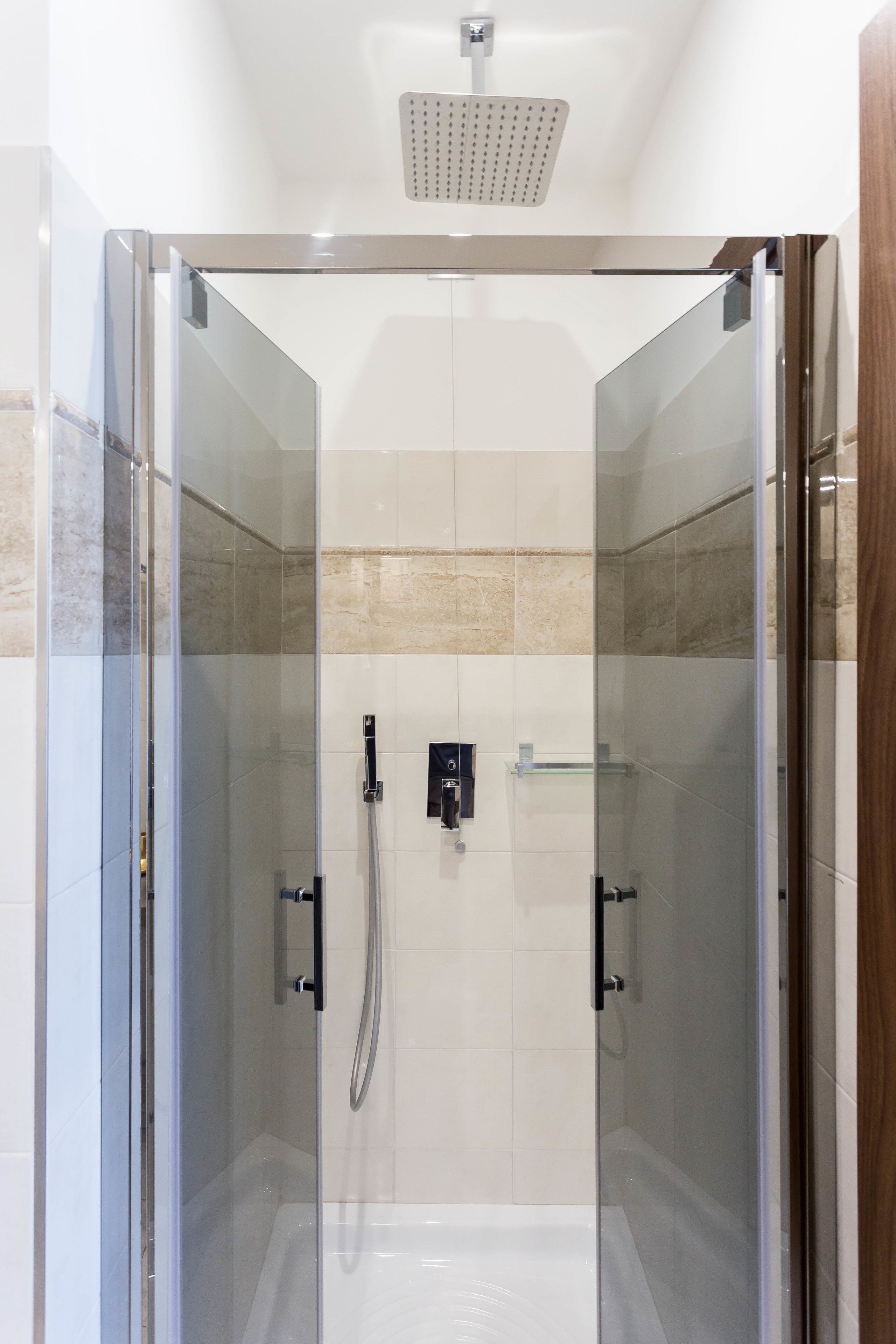 Ein modernes Duschbad mit Glaswänden, einer Handbrause und einer fest installierten Bedienarmatur.