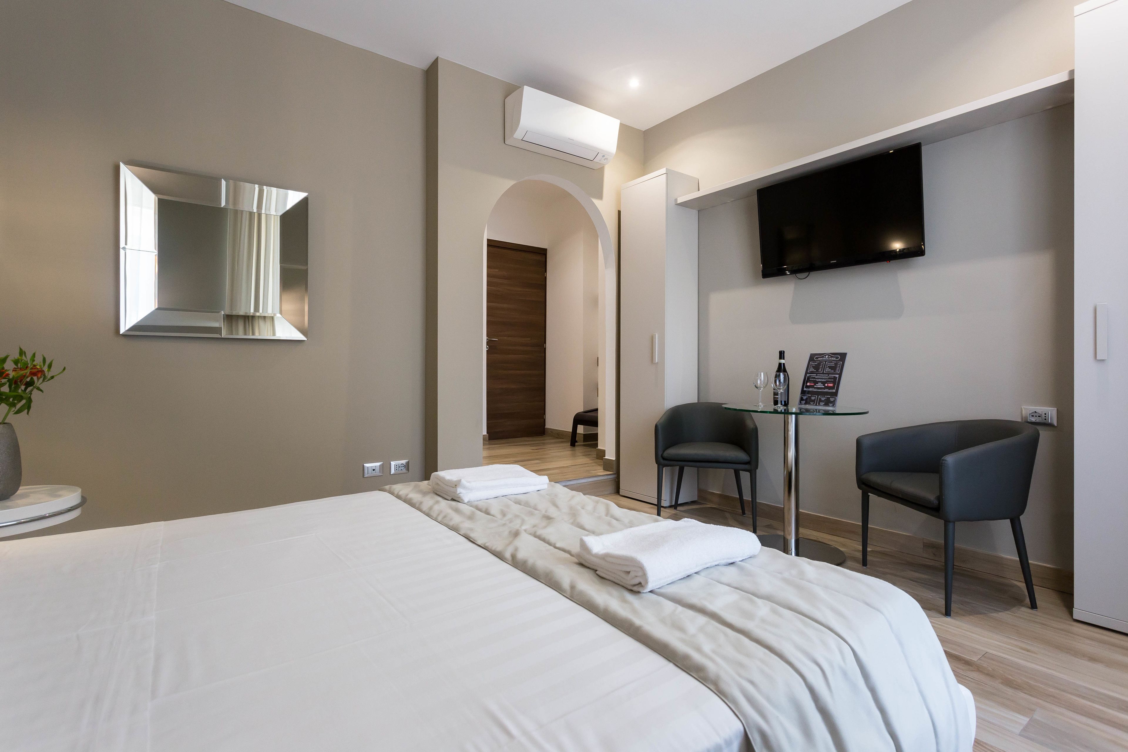 Une chambre d’hôtel moderne avec un grand lit, un téléviseur à écran plat fixé au mur, une petite table avec une chaise et un miroir au mur.