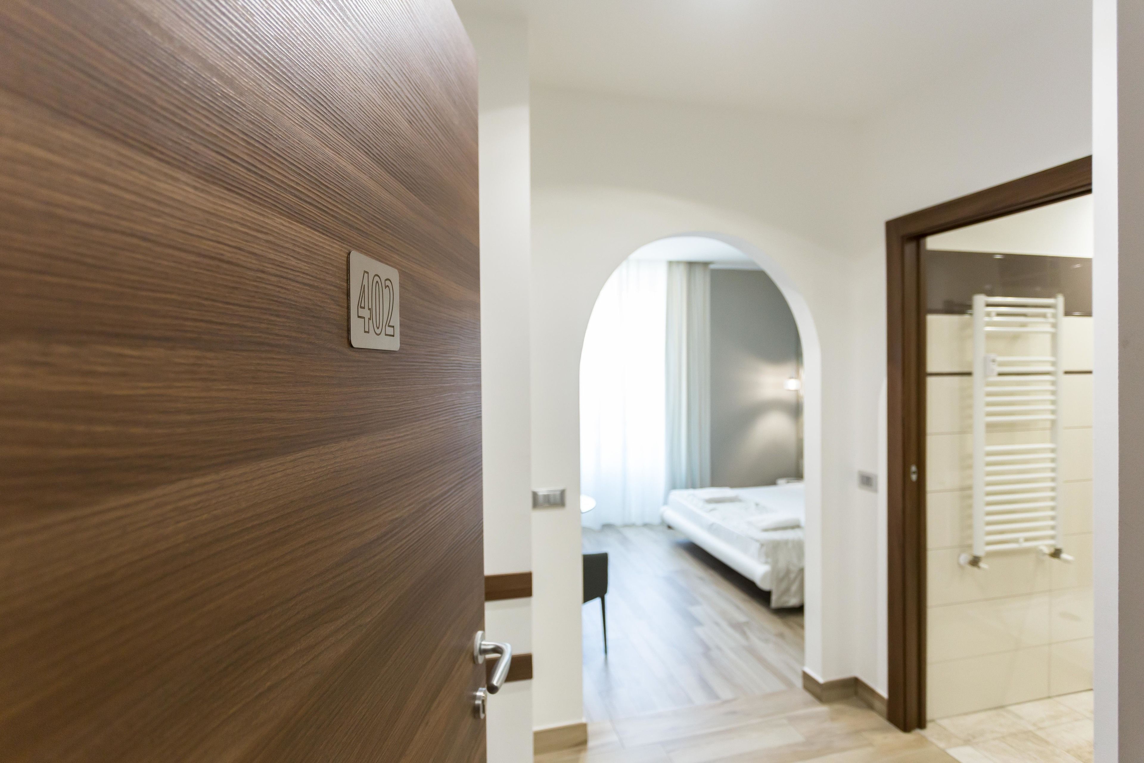 Une chambre d’hôtel avec une porte en bois portant le numéro « 402 », un lit, une chaise blanche et un porte-serviettes.