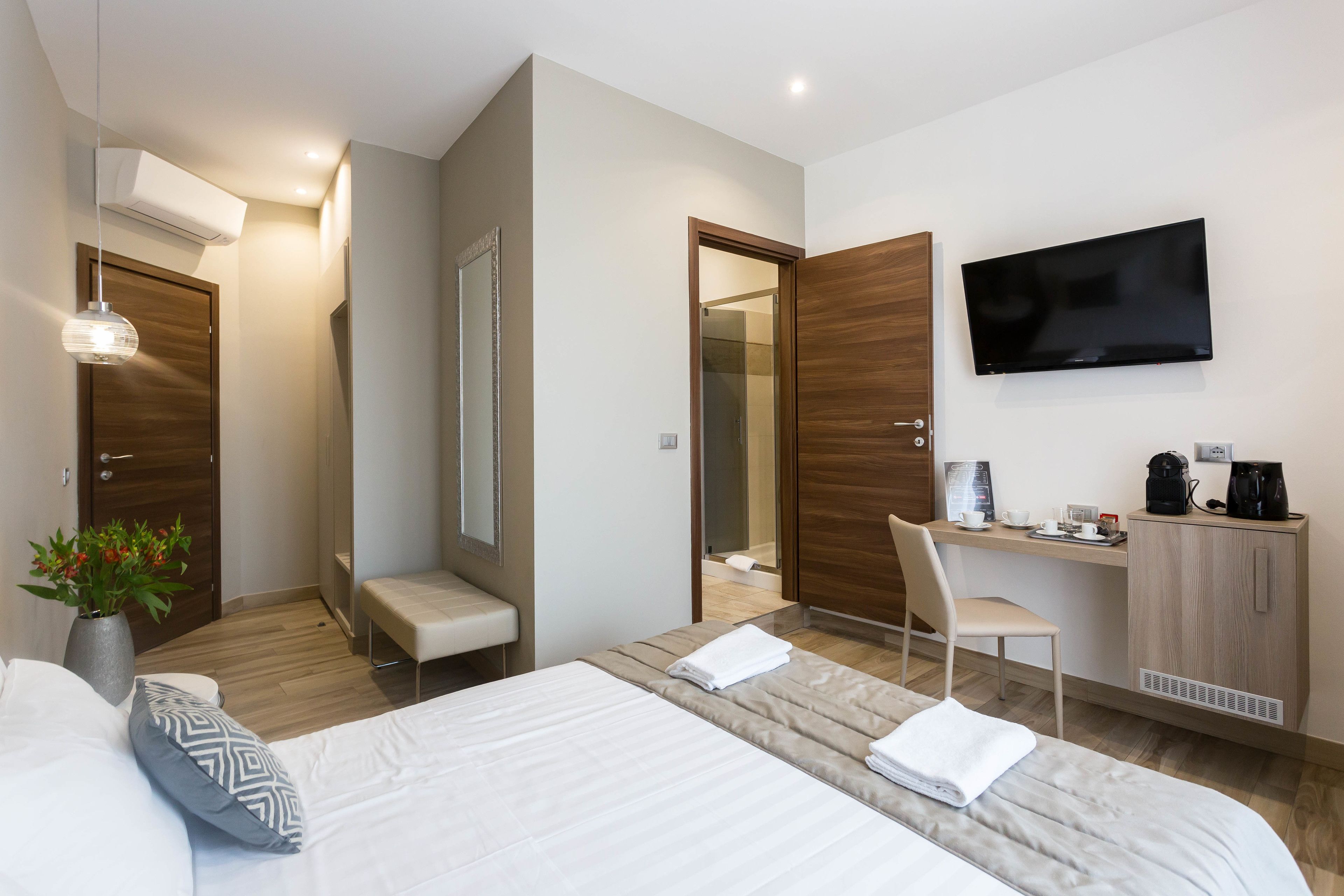 A modern hotel room with a large bed, a desk, a TV, and a coffee maker.