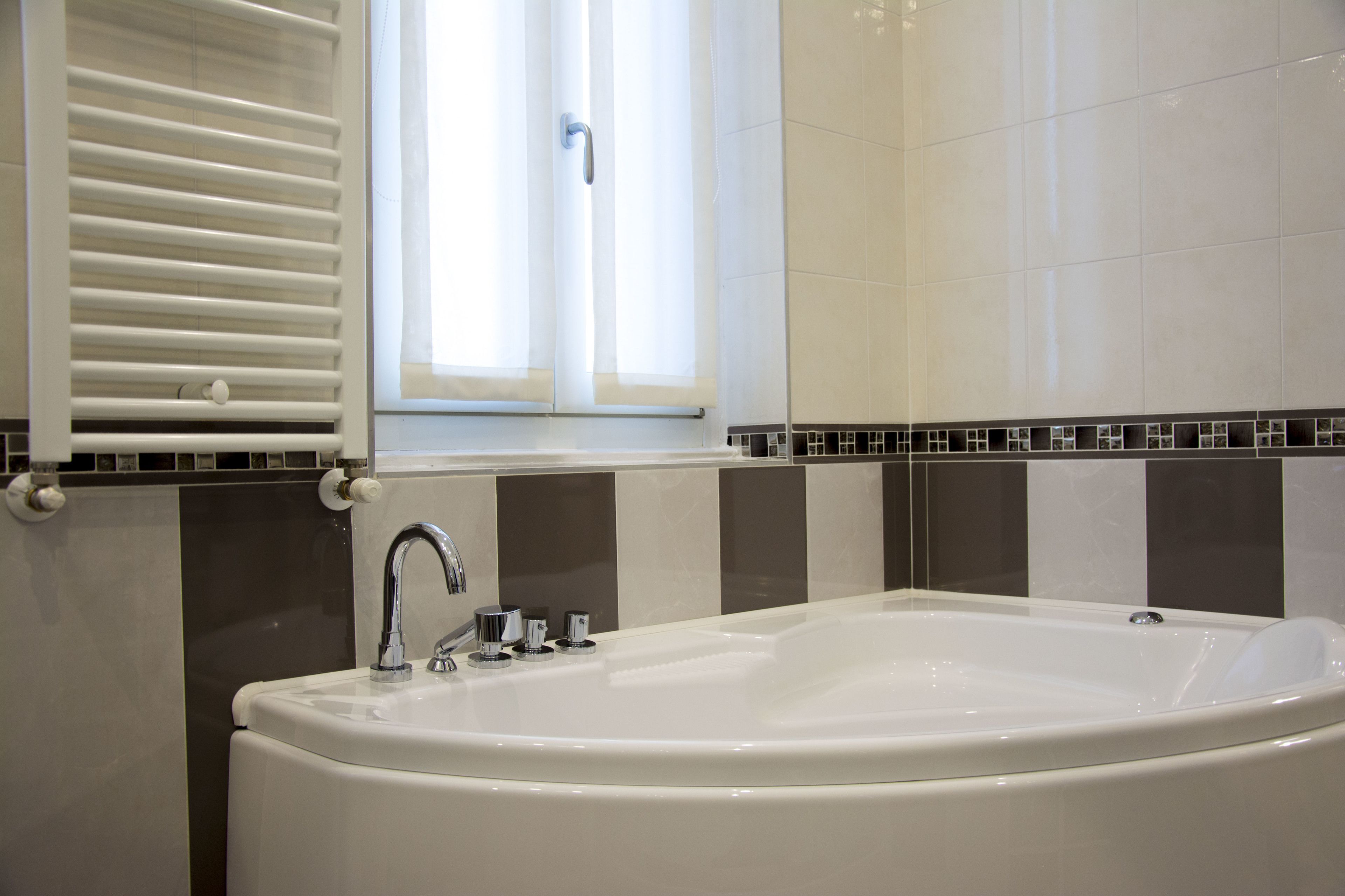 Une salle de bain moderne avec une baignoire sur pieds, une fenêtre avec stores et un mur recouvert de carreaux.