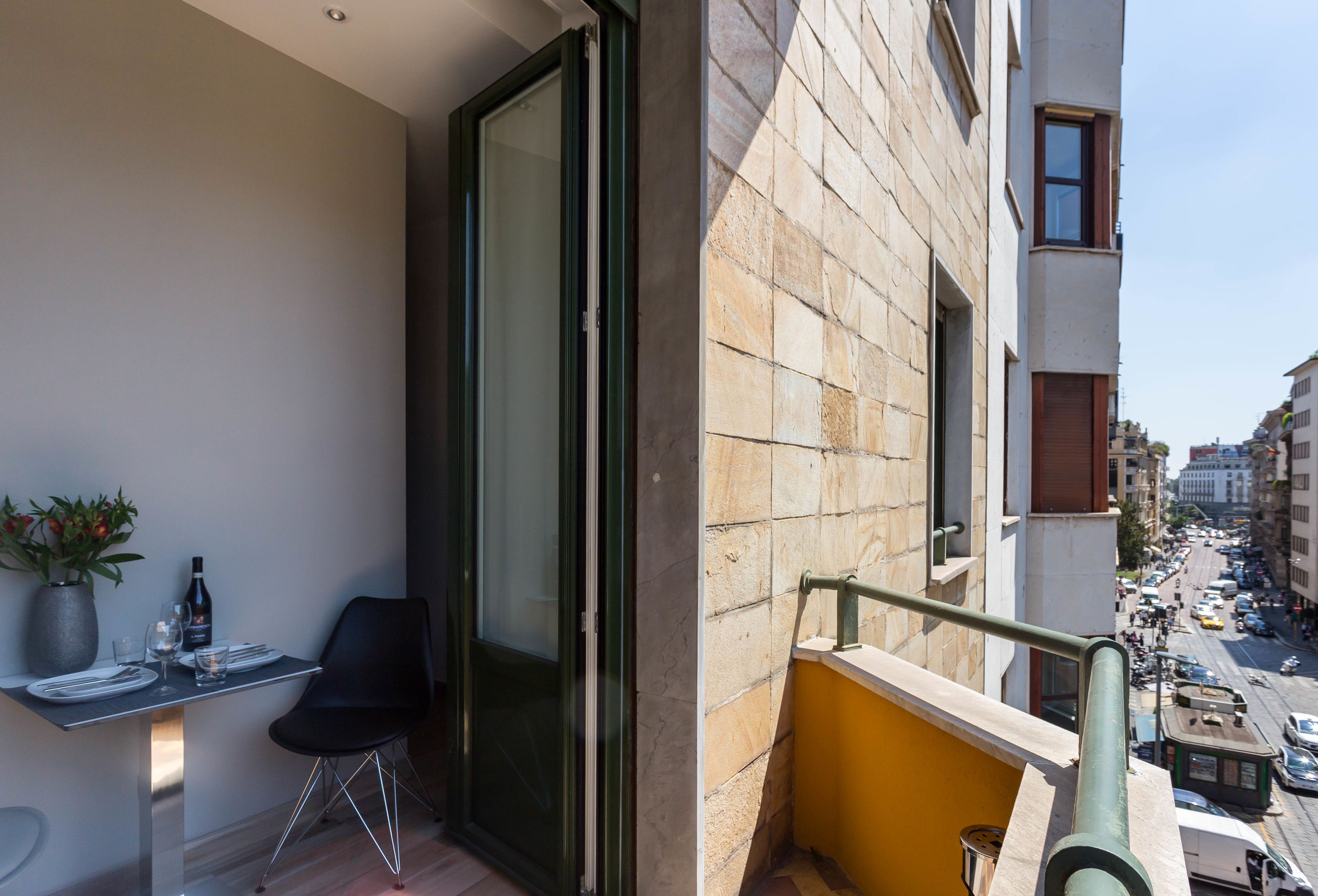 A balcony with a dining area, a potted plant, and a view of the street below.