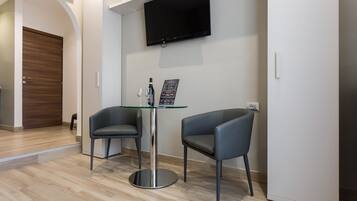 Una habitación moderna con una mesa de vidrio, dos sillas, un televisor de pantalla plana montado en la pared y una puerta de madera.