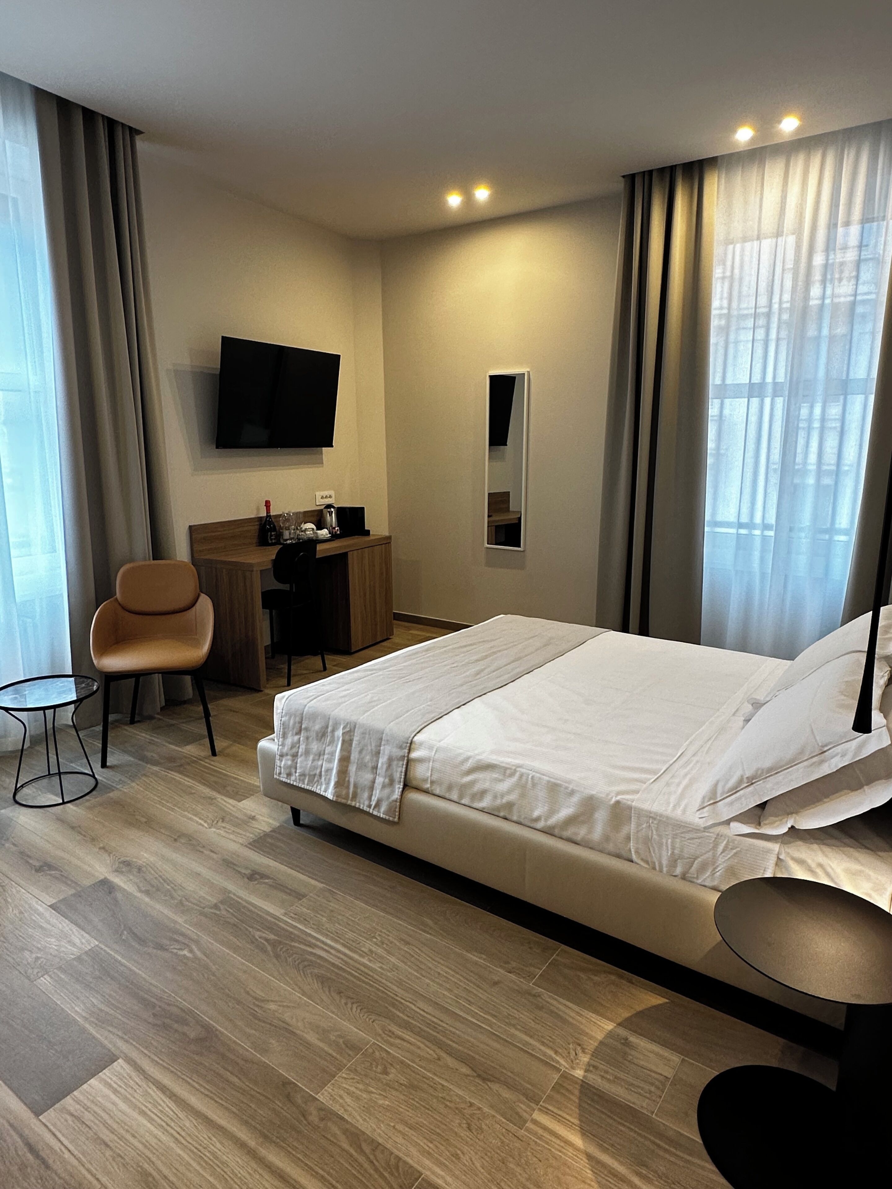 Ein Hotelzimmer mit einem Bett, einem Schreibtisch, einem Stuhl, einem Fernseher und einem Fenster mit Vorhängen.