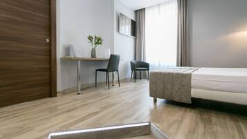 Une chambre d’hôtel moderne avec un plancher en bois, un lit, un bureau avec deux chaises, une télévision et une fenêtre avec des rideaux.