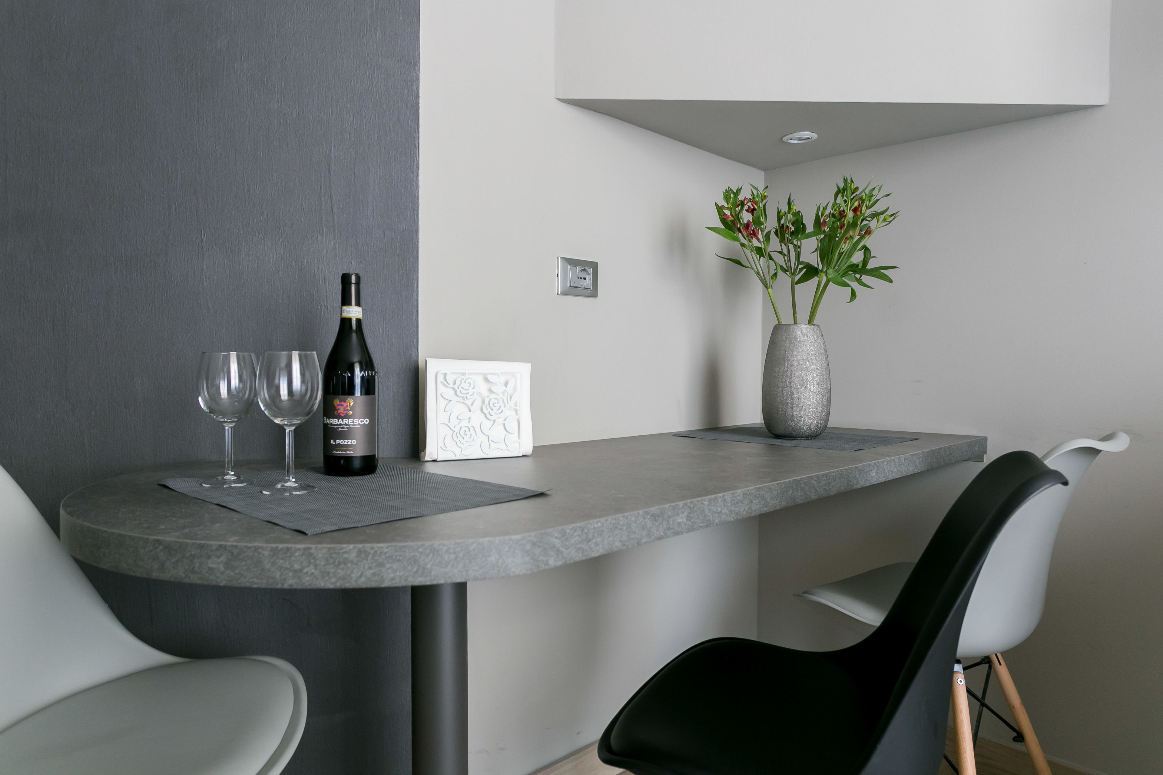 Een moderne eetruimte met een ronde tafel, twee wijnglazen, een wijnfles, een vaas met bloemen en een stoel.