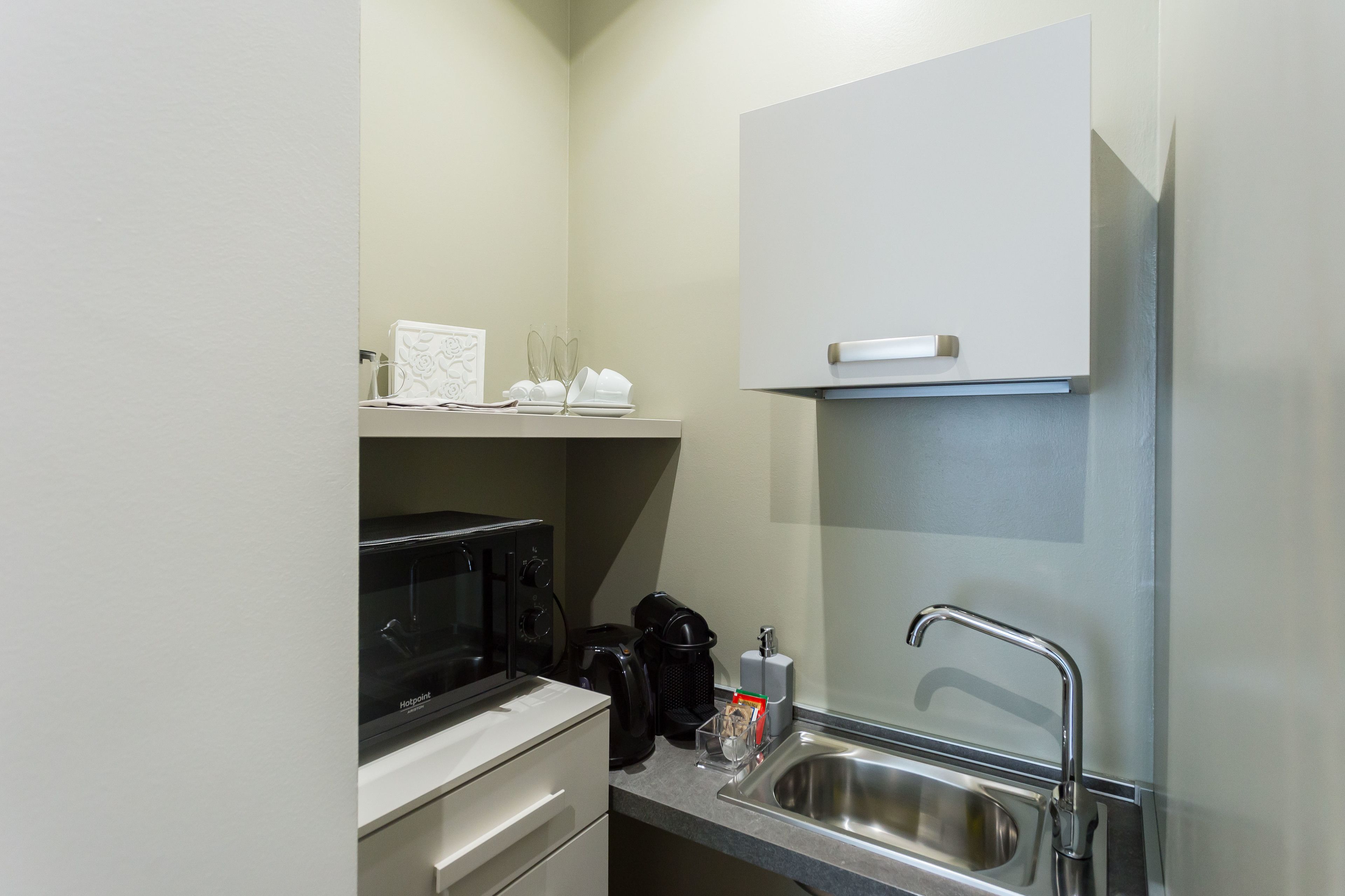 A compact kitchenette with a microwave, coffee maker, and a stainless steel sink.