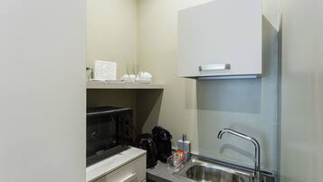 A compact kitchenette with a microwave, coffee maker, and a stainless steel sink.