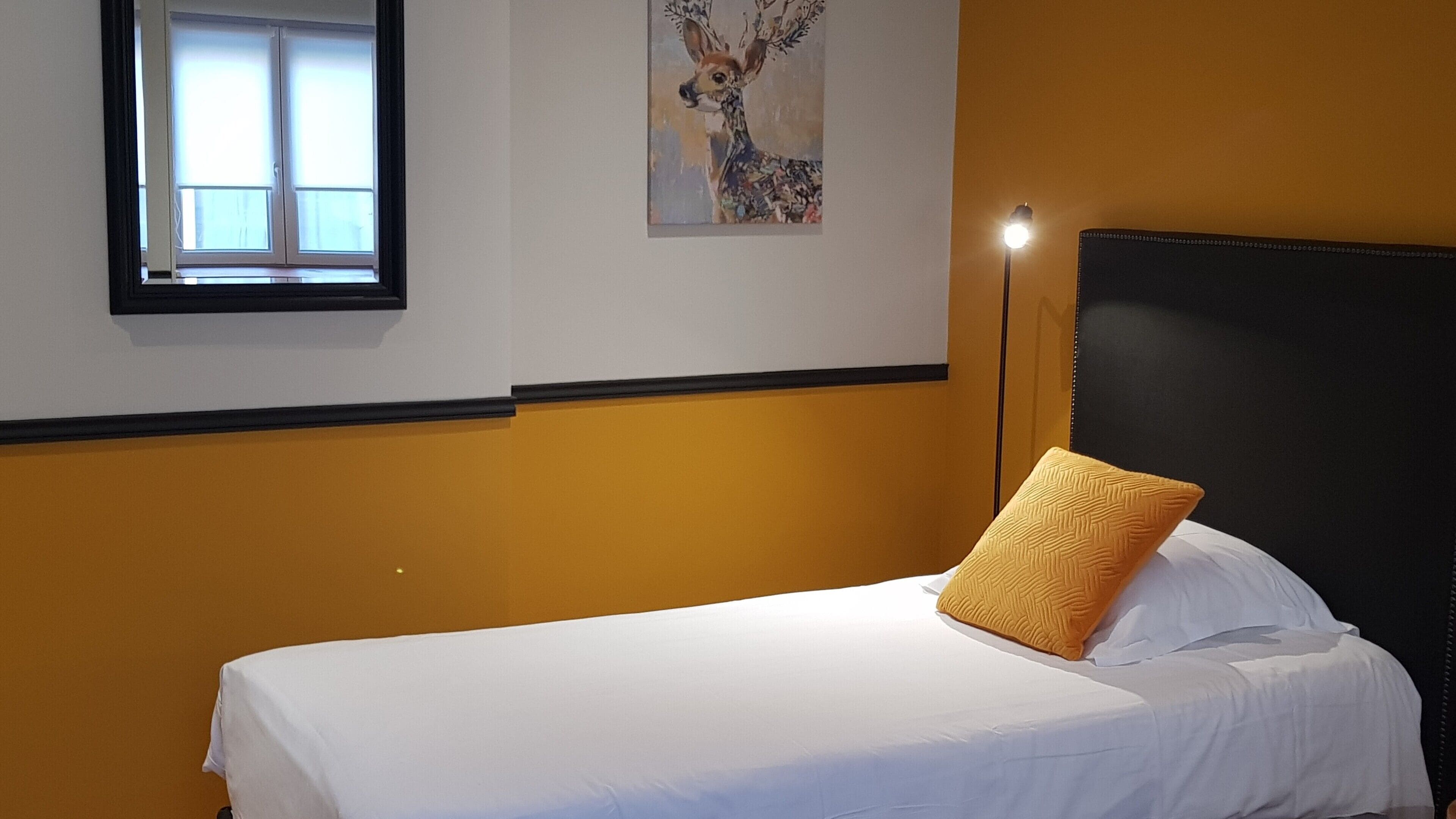 A hotel room with a bed, a window, and a painting on the wall.