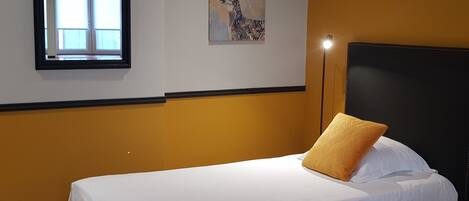 A hotel room with a bed, a window, and a painting on the wall.