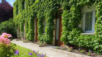 Un bâtiment à la façade en pierre, recouvert de lierre, et un chemin pavé menant à l’entrée.