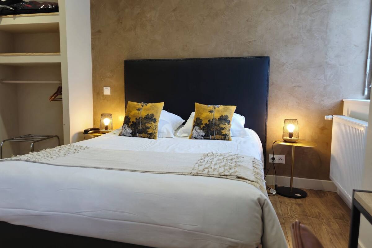A neatly made bed with white linens, two decorative pillows, bedside lamps, and a wooden floor.