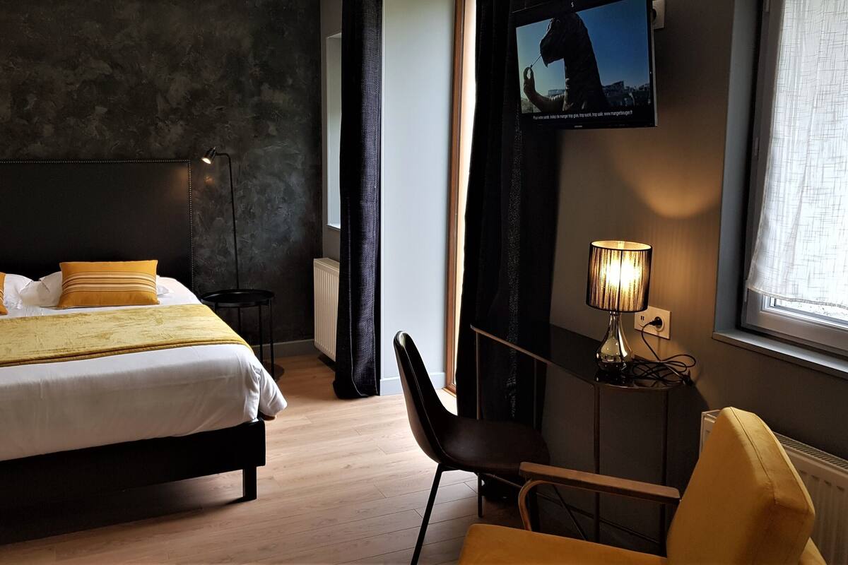 A hotel room with a bed, a chair, a lamp, a TV, and a window with curtains.