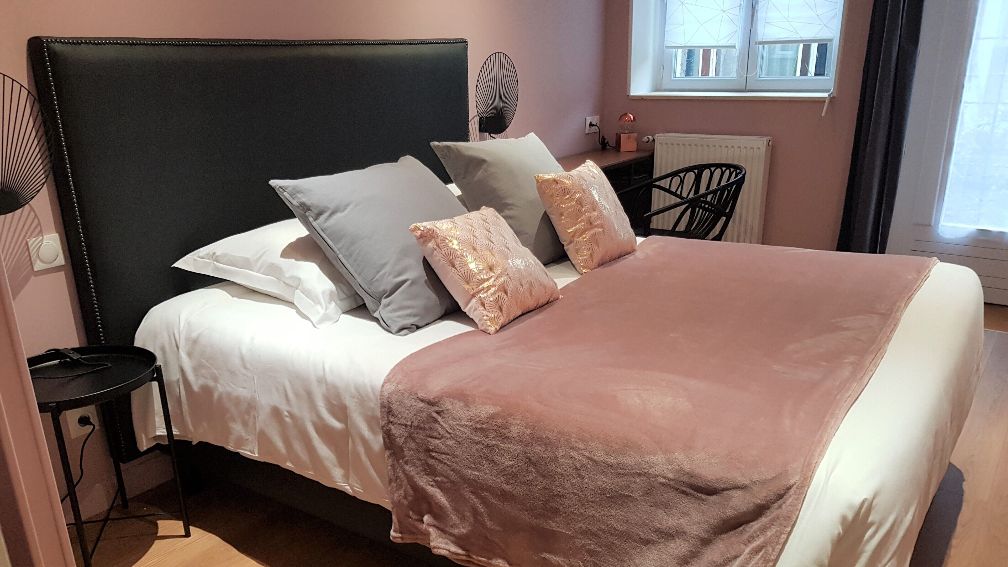 A neatly made bed with a black headboard, multiple pillows, and a pink blanket.