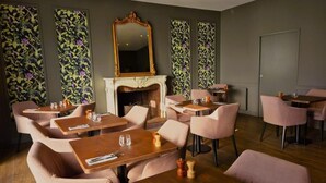 Un restaurant avec des tables en bois et des chaises roses, une cheminée et un papier peint à motifs floraux.