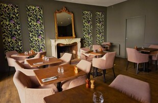 Un restaurant avec des tables en bois et des chaises roses, une cheminée et un papier peint à motifs floraux.